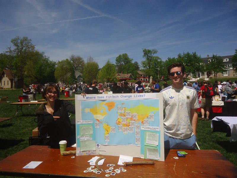Two members staffing the FinTech booth outdoors with a Where Does FinTech Change Lives poster