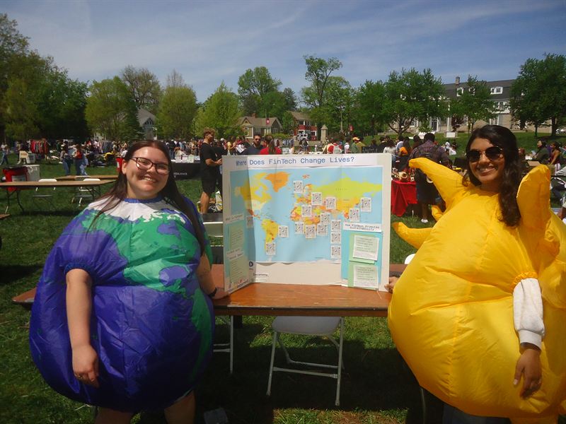 Two members in inflatable earth and sun costumes beside the booth poster