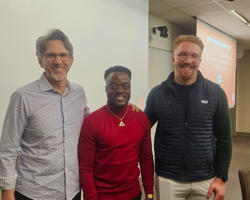 A member standing between two guest speakers at the front of a classroom